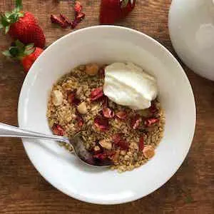 a bowl of muesli on a wooden board with dried strawberry pieces
