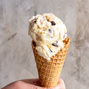 a hand holding an ice cream cone of cookie dough ice cream