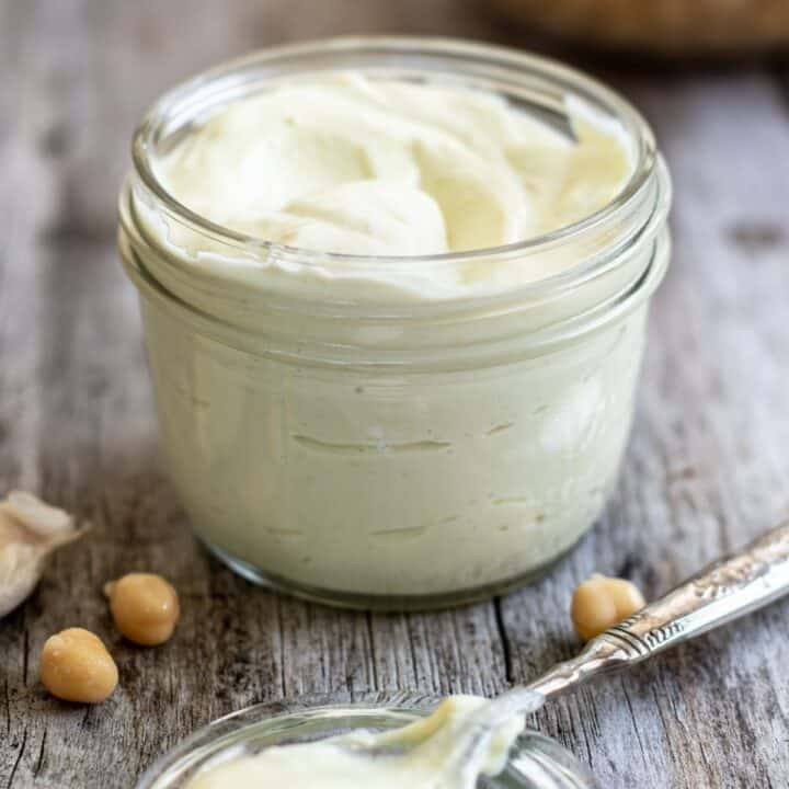 a close up of a jar of mayo with chickpeas on a wooden board.