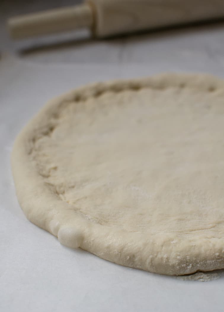 a sourdough pizza base rolled out into a pizza shape on a white bench