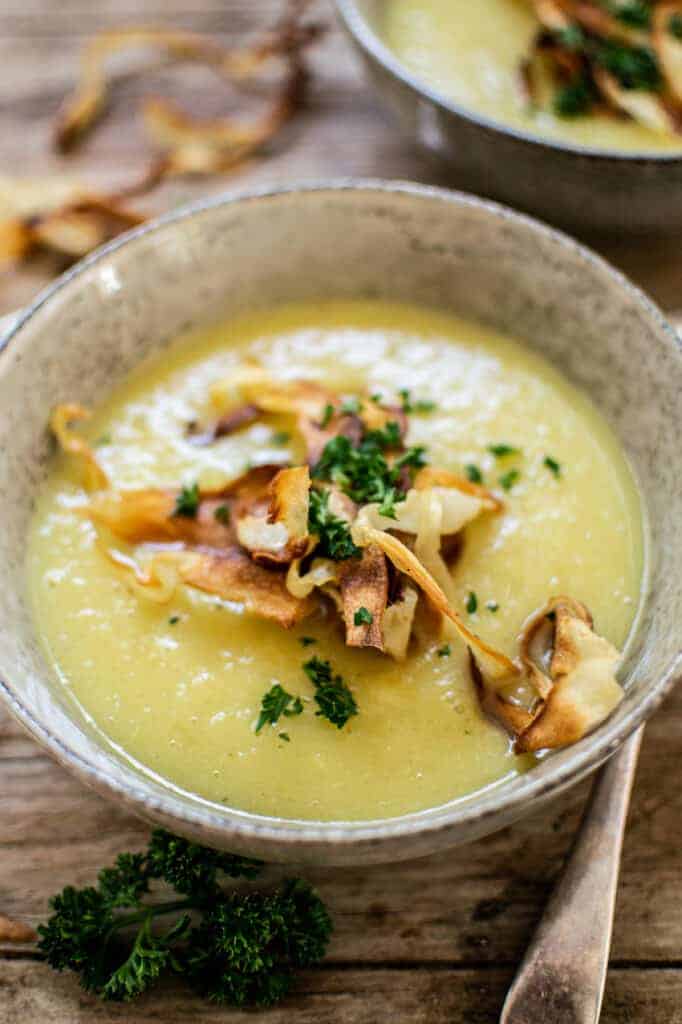 a side angle of a grey bowl of parsnip soup on a wooden bench, topped with parsley and parsnip chips 
