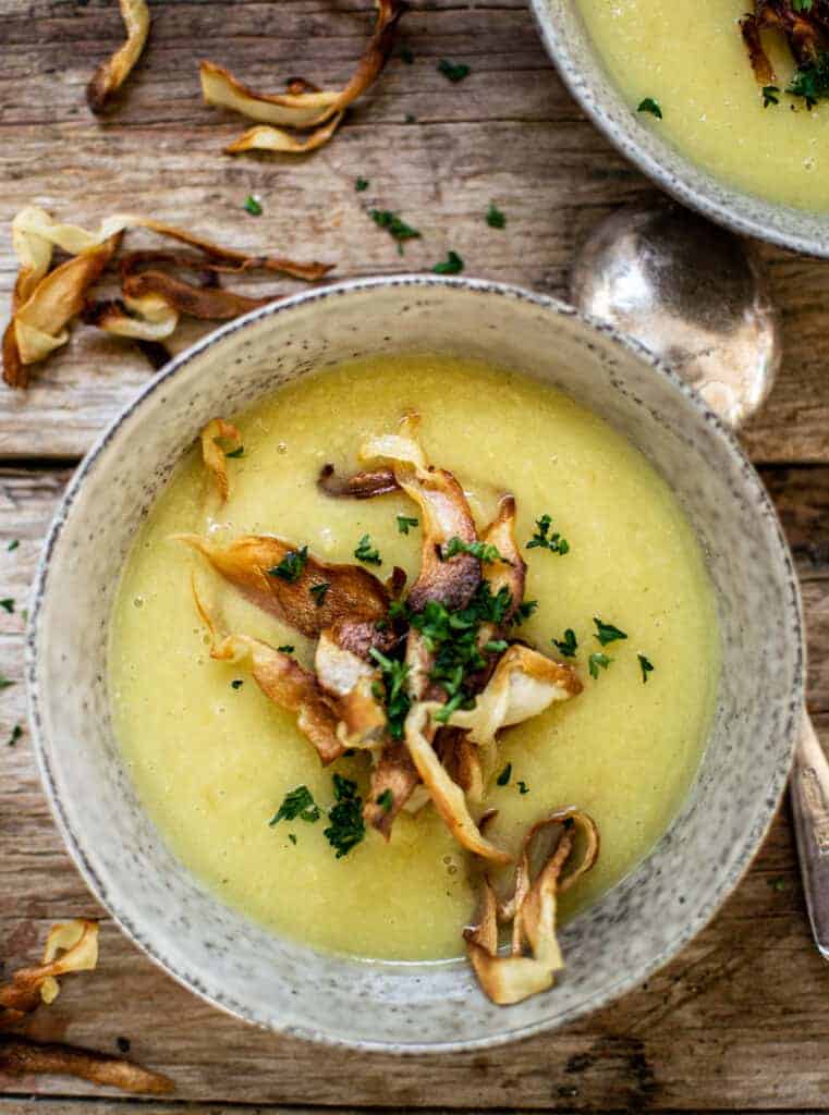 a grey bowl of parsnip soup on a wooden bench, topped with parsley and parsnip chips 