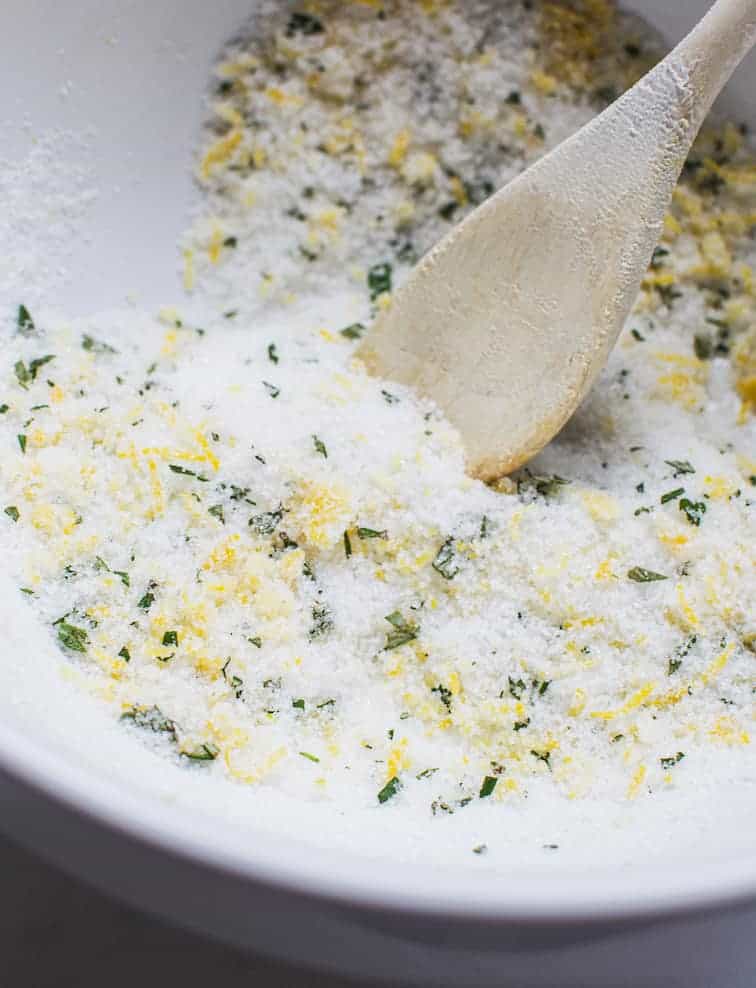 a wooden spoon stirring sugar and lemon zest and rosemary 