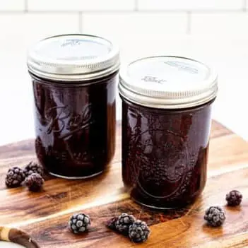 two jars of blackberry jam on a wooden board