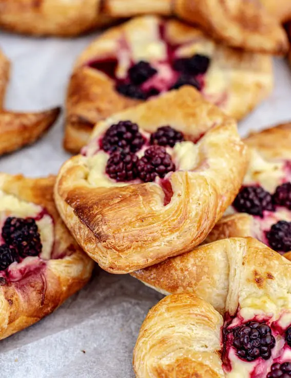 a pile of sourdough Danish pastries on baking paper. The pastries all have blackberries and cream cheese on them