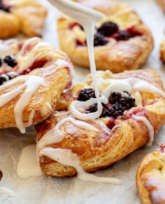 white icing being drizzled on pastries from a fork, with blackberries on them