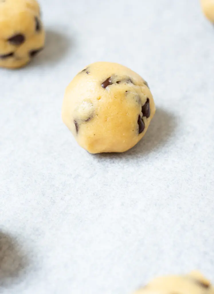 a close up of an unbaked cookie dough ball on white parchment paper