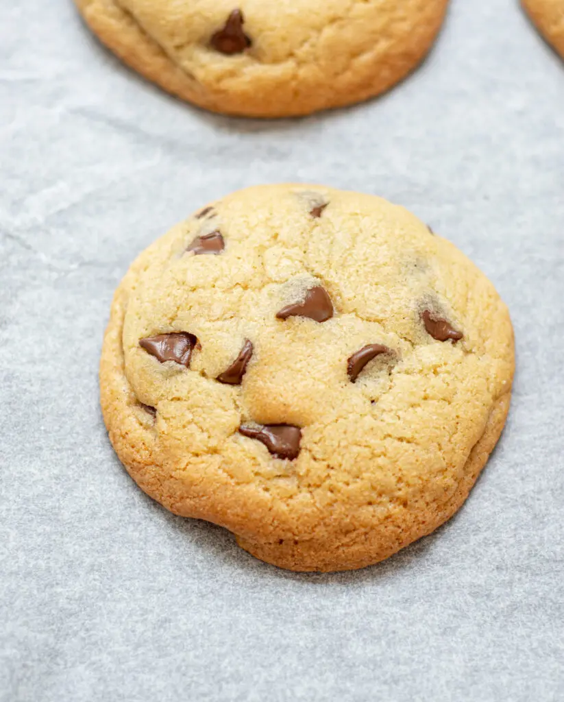 a close up of a baked chocolate chip cookie on white parchment paper