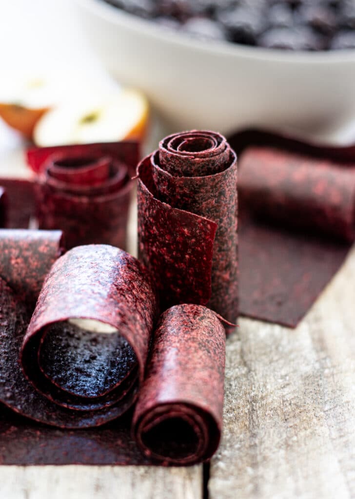 fruit leather rolls on a wooden board with a bowl of berries in the background