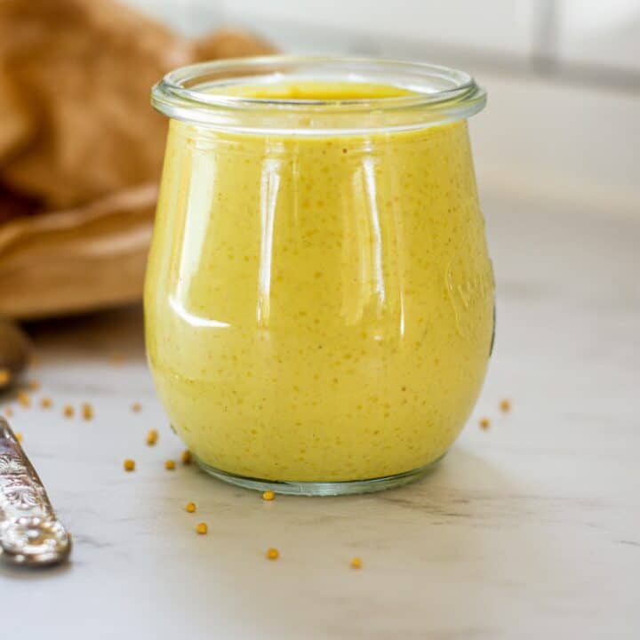 a jar of yellow mustard on a white bench.