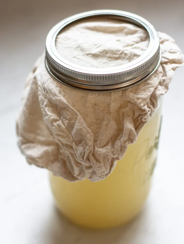 a jar of apple cider vinegar covered with a cloth and silver band 