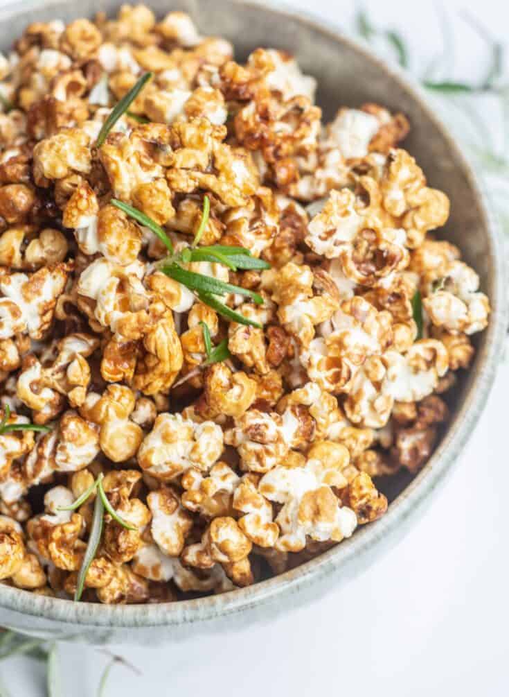 a close up of a bowl of caramel popcorn with green rosemary