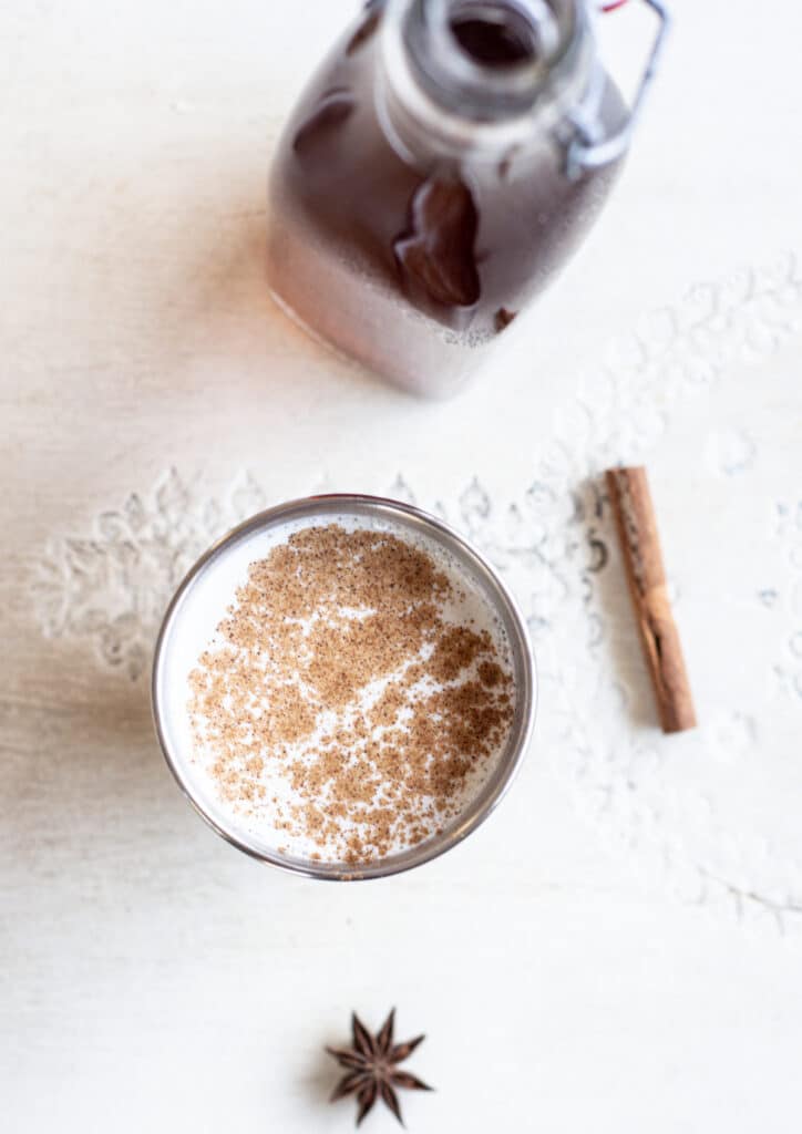 a silver cup of white milk with cinnamon sprinkled on top a cinnamon stick and star anise in the background