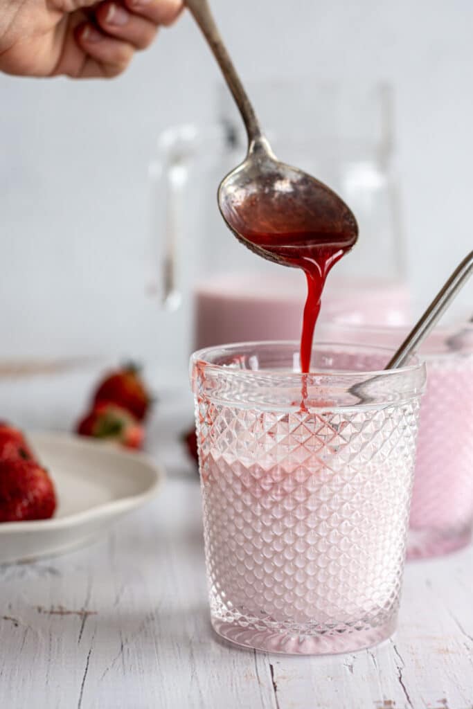 strawberry syrup poured into a glass of milk
