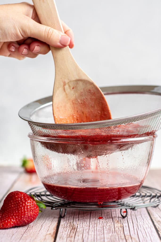 a spoon stirring strawberry sauce over a sieve