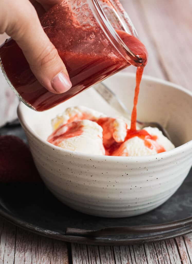 a jar of strawberry sauce poured over ice cream
