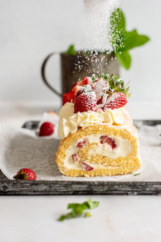 strawberry swiss roll with powdered sugar being dusted on it