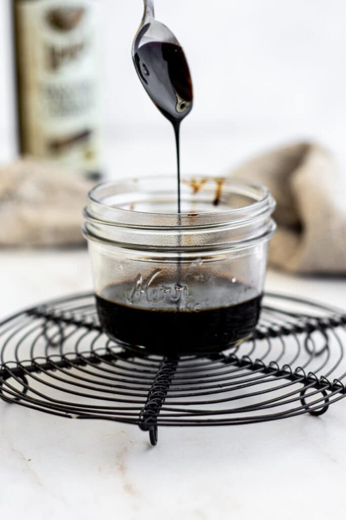 a spoon drizzling balsamic glaze in a jar on wire rack