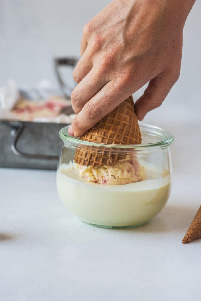 a hand dipping ice cream into white chocolate.